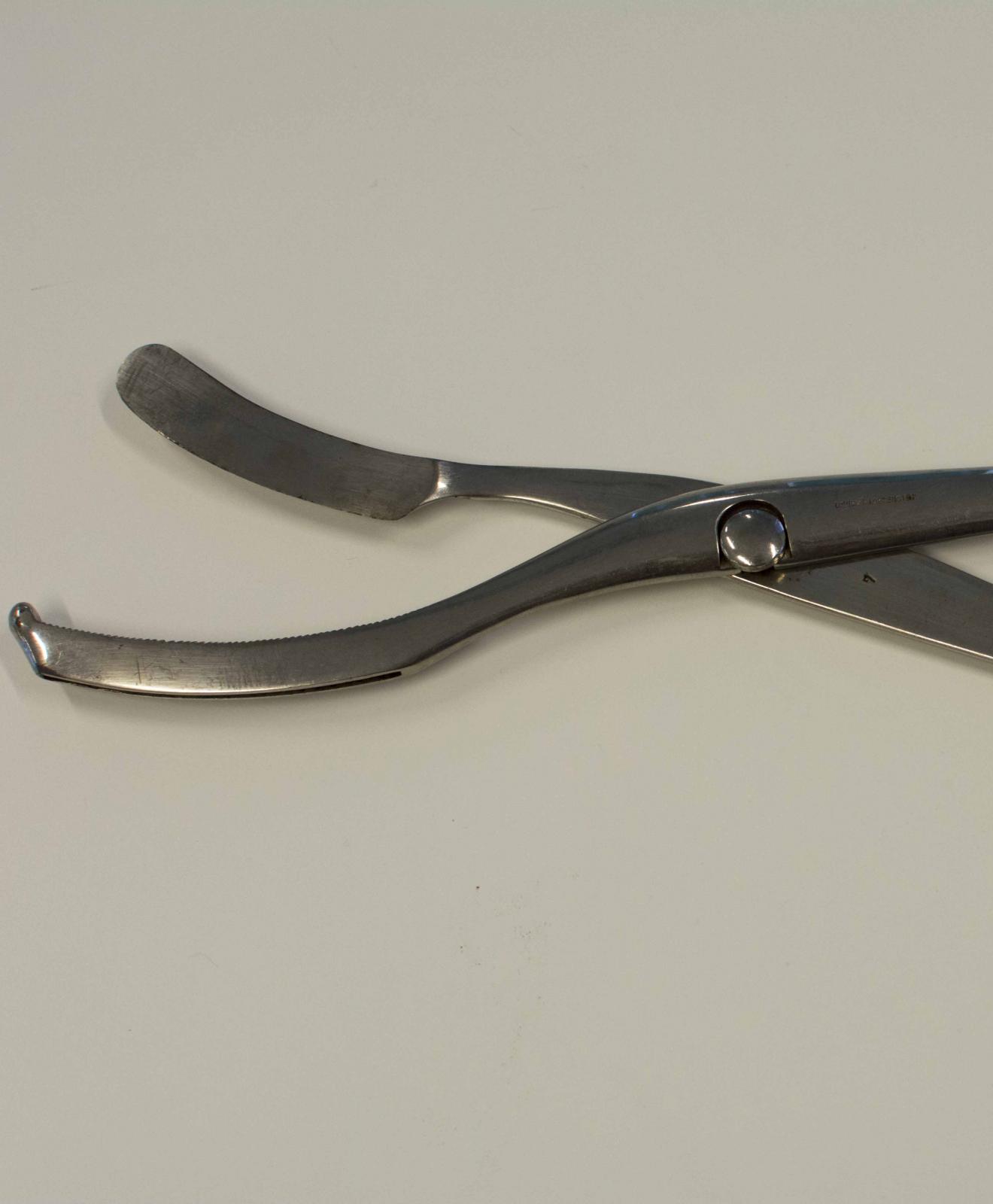 Instrumento metálico con forma de tijera, empuñadura simple y cabeza cortante terminada en forma curva en uno de sus extremos