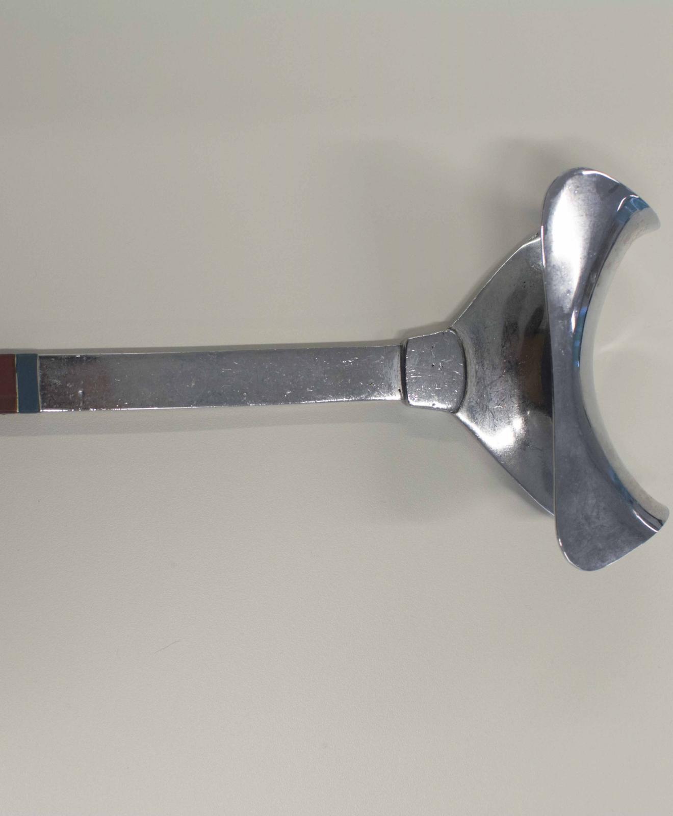 Instrumento metálico con forma de pala. Un extremo presenta forma de ancla, rematado con un aro y el extremo cuenta con una estructura cóncava