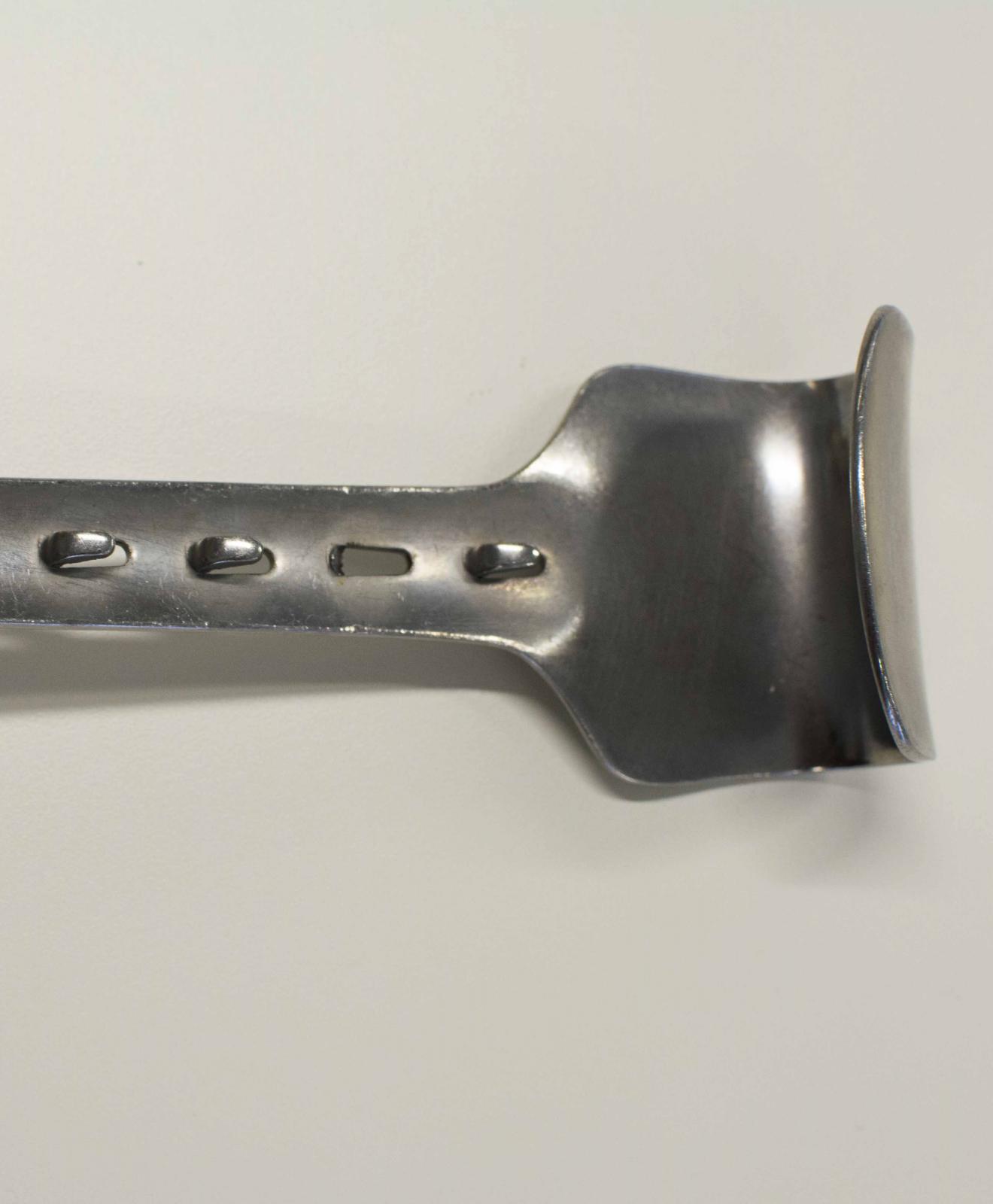 Instrumento metálico con forma de espátula, con el eje transversal perforado, un extremo convexo y otro cóncavo