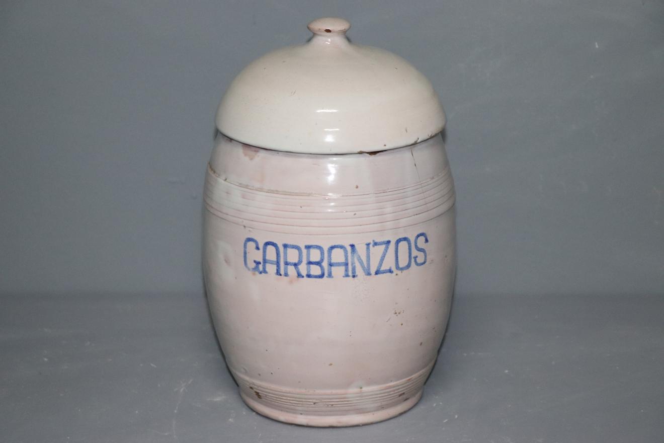 Recipiente con forma de barril, tapado por una pieza semiesférica, en el que se lee la palabra "GARBANZOS" en azul sobre el esmalte blanco 