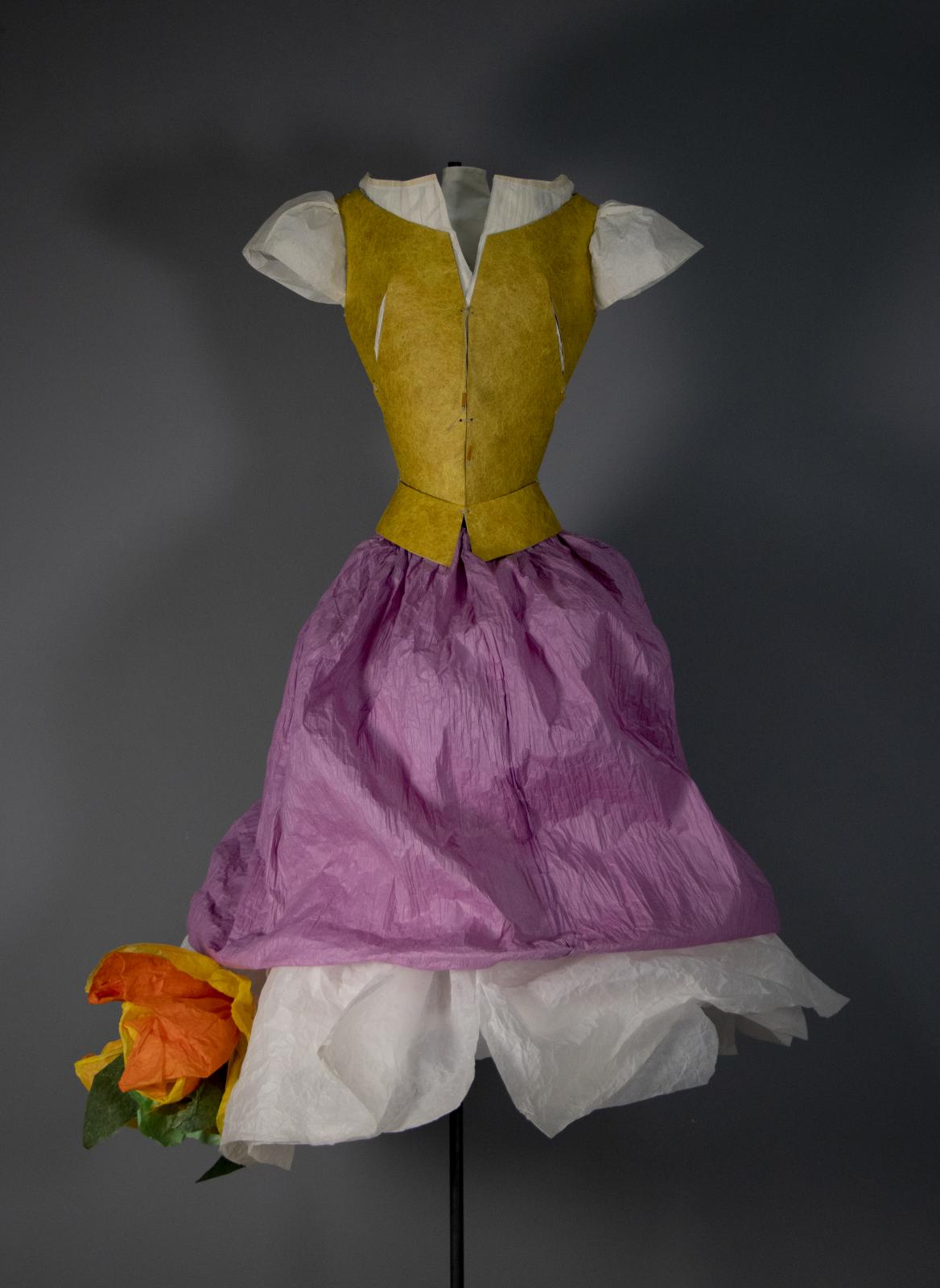Vestido escultura realizado con papel y cartulina, compuesto de corpiño y blusa de manga corta, y una falda con faldón decorada con una flor de vivos colores